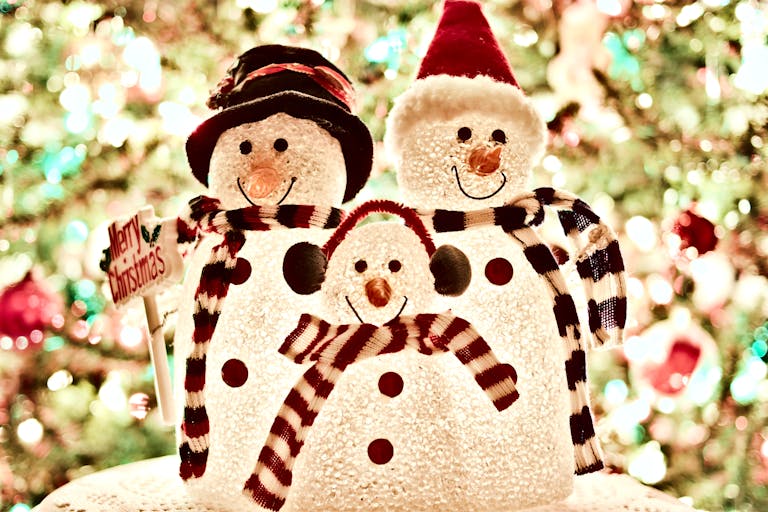 Close-up of a cheerful snowman family decoration with bright Christmas lights in the background.